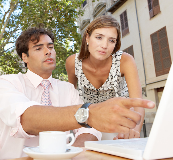 Geschäftskollegen schauen auf einen Laptop-Bildschirm, während sie ein Meeting auf der Terrasse eines Cafés haben - Foto, Bild