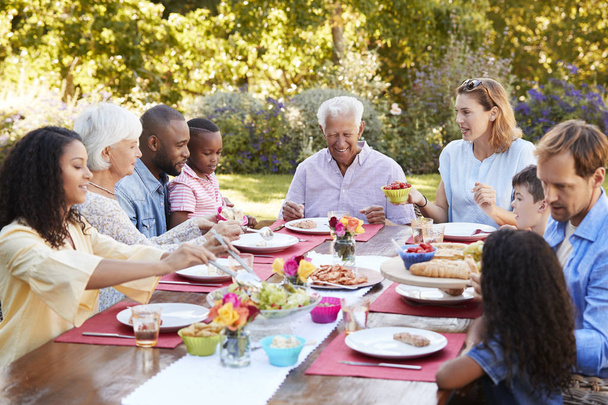 Οικογένεια και τους φίλους που σερβίρει μεσημεριανό γεύμα στο τραπέζι στον κήπο - Φωτογραφία, εικόνα