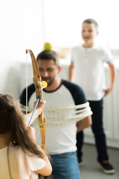 selective focus of children playing with tied father and pretending shooting with toy bow at home - Fotoğraf, Görsel