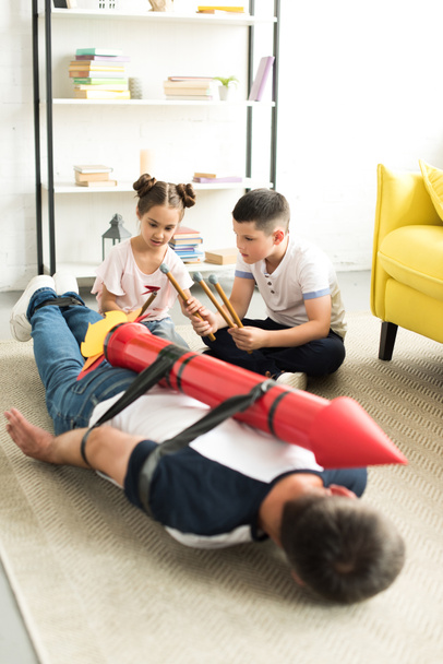 tied dad with rocket toy lying on floor and children playing with him  - Photo, Image