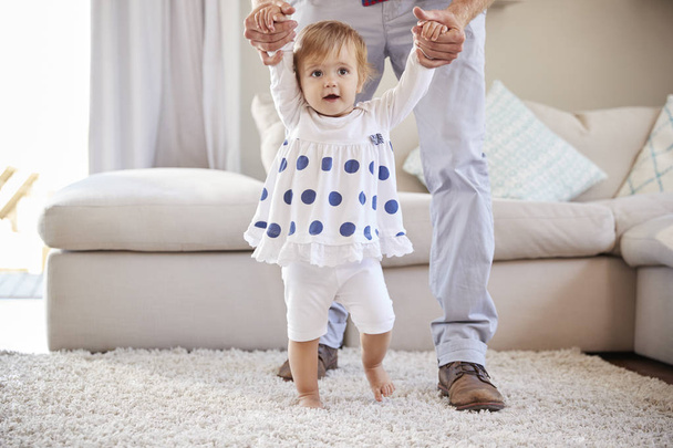 Father helping daughter learning to walk in sitting room - Photo, image