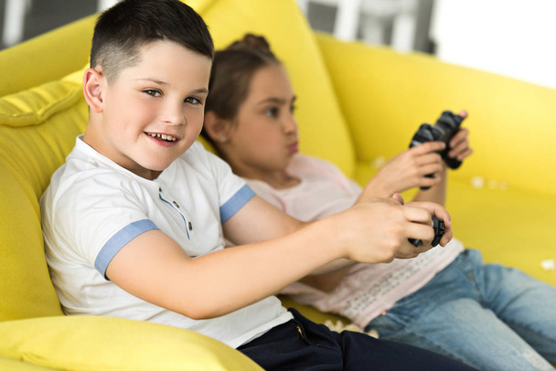 сестра и брат играют в видеоигры на диване дома
 - Фото, изображение
