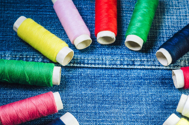 Катушки цветных нитей, расположенные по кругу на джинсовой ткани
 - Фото, изображение