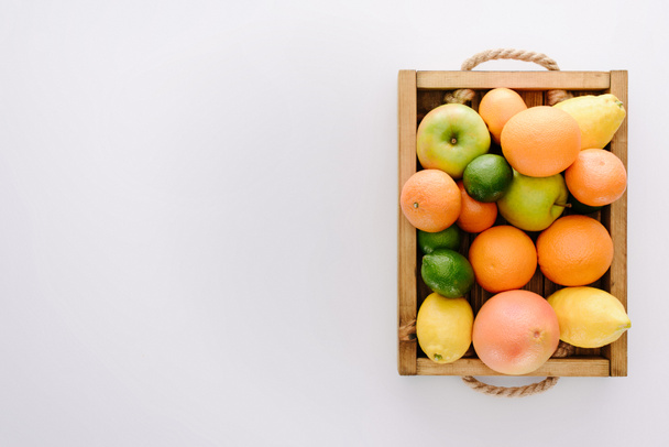 верхний вид различных спелых фруктов в деревянной коробке на белой поверхности
 - Фото, изображение