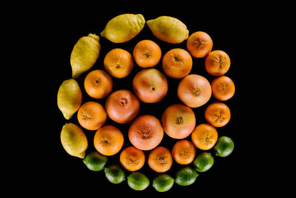 bovenaanzicht van verschillende citrusvruchten samenstelling in spiraalvorm geïsoleerd op zwart - Foto, afbeelding