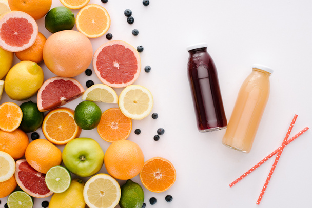 top view of various citrus fruits and blueberries with bottles of juice on white tabletop - Photo, Image