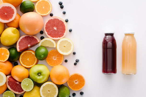 vista superior de frutas cítricas com mirtilos e garrafa de suco fresco na superfície branca
 - Foto, Imagem