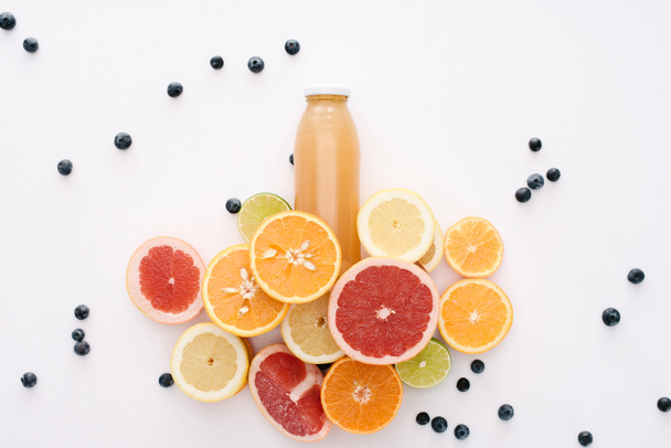 vista superior de garrafa de suco com fatias de frutas cítricas e mirtilos na superfície branca
 - Foto, Imagem
