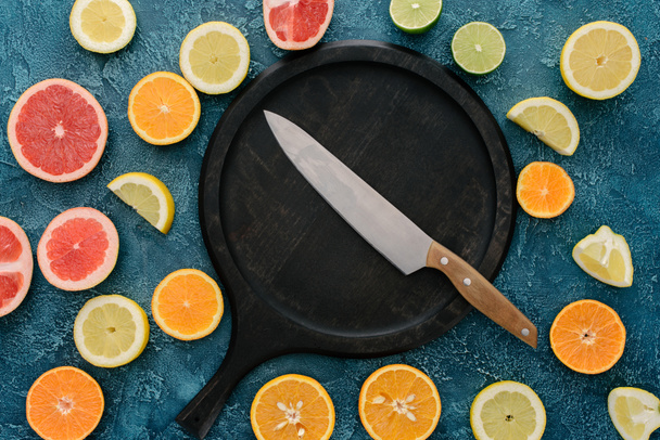 top view of plate in shape of skillet and knife surrounded with citrus fruits slices on blue concrete surface - Photo, Image