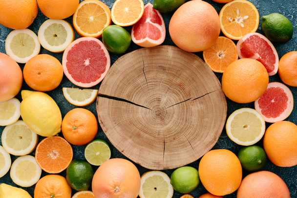 top view of wooden slice surrounded with citrus fruits slices on blue concrete surface - Photo, Image