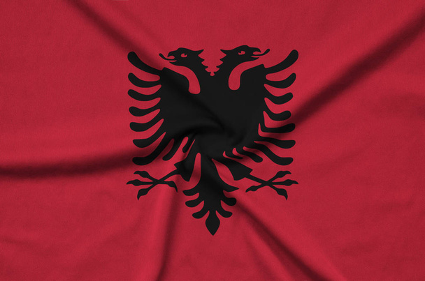  アルバニアの国旗は、多くのひだとスポーツの布生地に描かれています。スポーツ チームを振ってバナー - 写真・画像