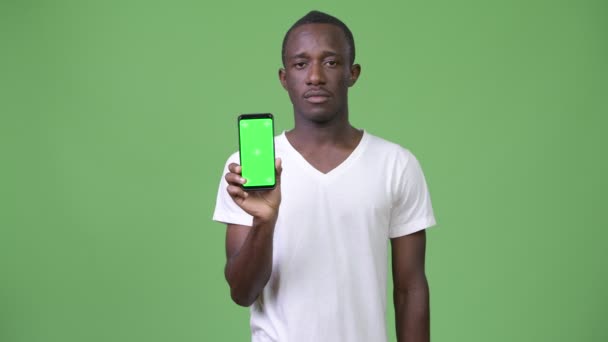 Young African man showing phone against green background - Záběry, video