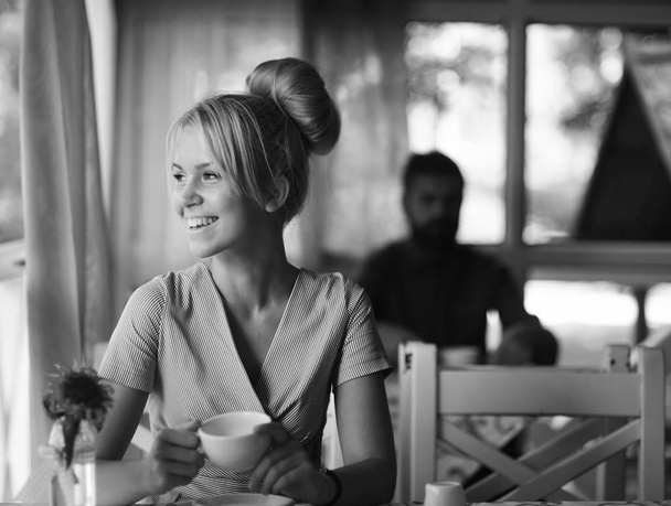 Woman with smiling face has hot beverage. Girl with blond hair in bun on light cafe background - Fotografie, Obrázek