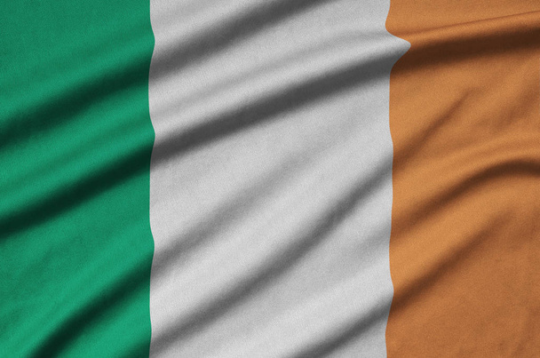 Írország lobogója alatt sok ráncok sport szövet szövet ábrázolja. Sport csapat integetett zászló - Fotó, kép