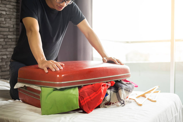 ο άνθρωπος προσπαθεί να χωρέσει όλα τα ρούχα για τη συσκευασία κόκκινη βαλίτσα του πριν από τις διακοπές - Φωτογραφία, εικόνα