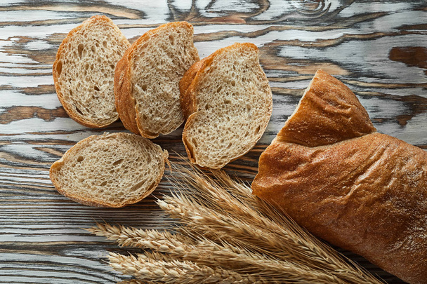 Crusty sliced bread wheat ears on wooden surface - Fotó, kép