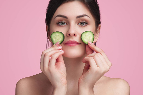 Woman holding slices of cucumbers on face - Fotografie, Obrázek