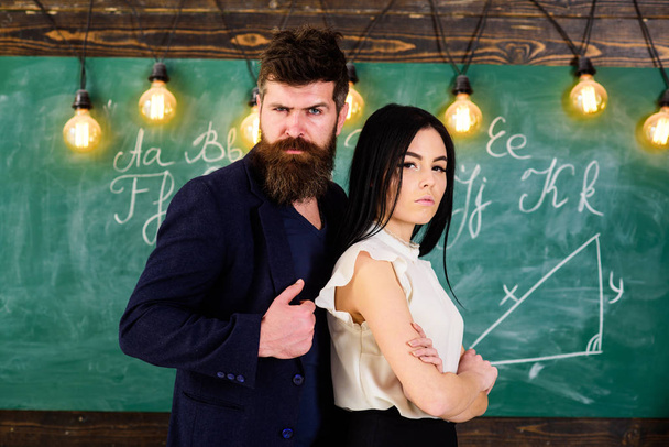 Teacher and strict schoolmaster look confident. Lady and hipster working together in school. Man with beard and sexy girl teacher stand in classroom, chalkboard on background. Partners concept. - Foto, Bild