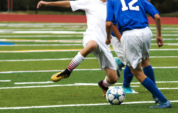 Teo chicos de secundaria compiten entre sí por el control de una pelota de fútbol durante un partido en un campo de césped verde
. - Foto, Imagen