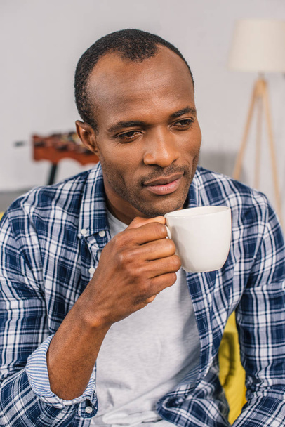 pensive young african american man holding coffee cup at home - Fotografie, Obrázek