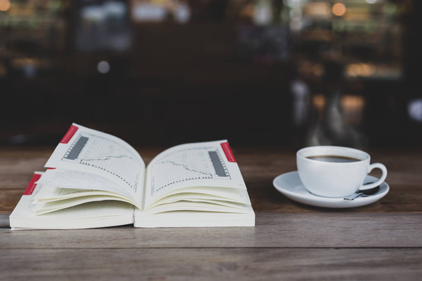 Open boek met kop koffie op houten tafel in matte kleur - Foto, afbeelding