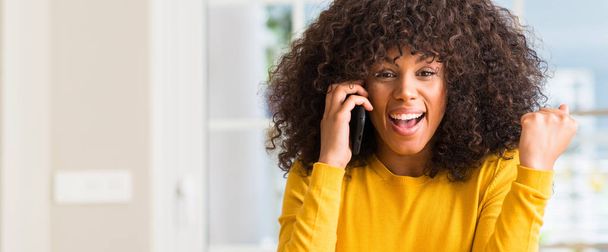 Mujer afroamericana usando teléfono inteligente gritando orgulloso y celebrando la victoria y el éxito muy emocionado, animando emoción
 - Foto, Imagen