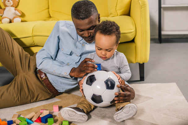 glücklicher Opa und kleiner Enkel spielen zu Hause mit Fußball und bunten Blöcken  - Foto, Bild
