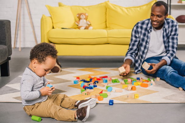 smiling young father looking at adorable child playing with colorful blocks at home - Foto, Imagen