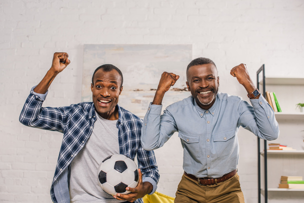 alegre padre e hijo adulto con pelota de fútbol triunfando y sonriendo a la cámara
  - Foto, Imagen