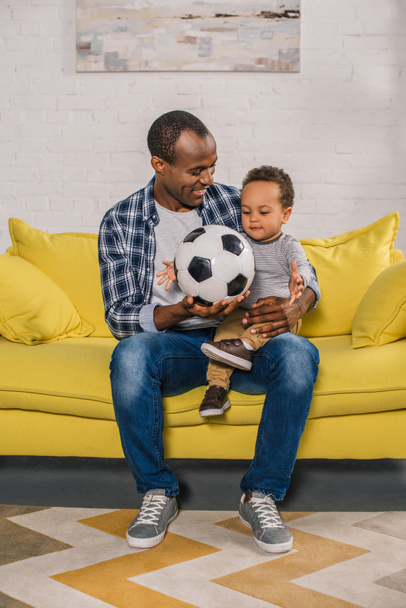 feliz joven padre sosteniendo pelota de fútbol y mirando lindo sonriente hijo
 - Foto, Imagen