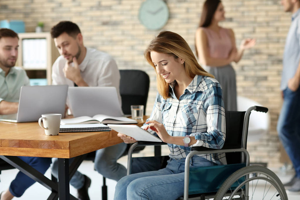 Young woman in wheelchair and colleagues at workplace - Photo, Image