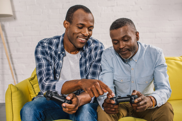 happy african american father and adult son using joysticks together at home - Foto, Imagem