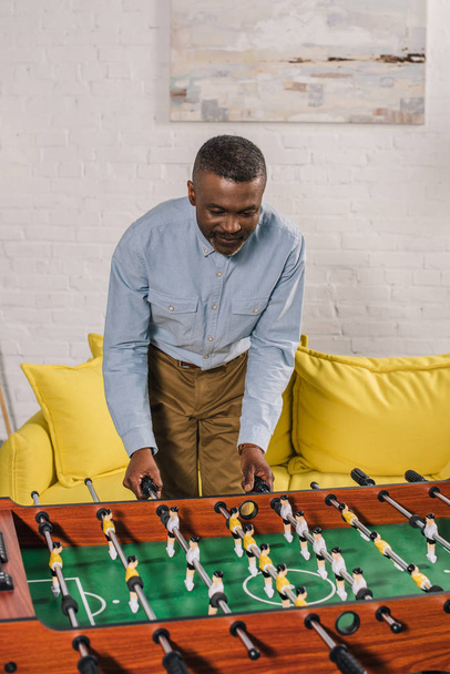 lachende Afro-Amerikaanse man voetballen tafel thuis - Foto, afbeelding