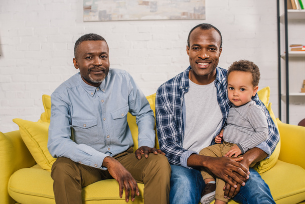happy african american father, grandfather and child sitting together and looking at camera - Zdjęcie, obraz
