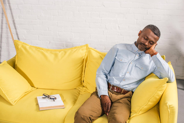 senior african american man sleeping on couch, book and eyeglasses on sofa - Фото, зображення