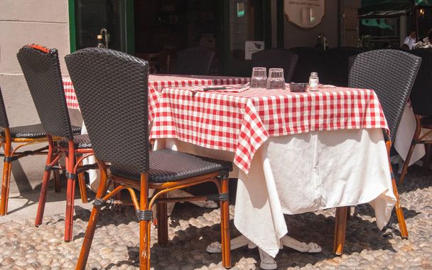 Conjunto de mesa com toalha de mesa quadriculada vermelha e branca fora de uma trattoria característica de Milão
 - Foto, Imagem