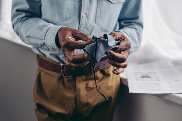 cropped shot of senior african american man cleaning eyeglasses with cloth - Фото, изображение