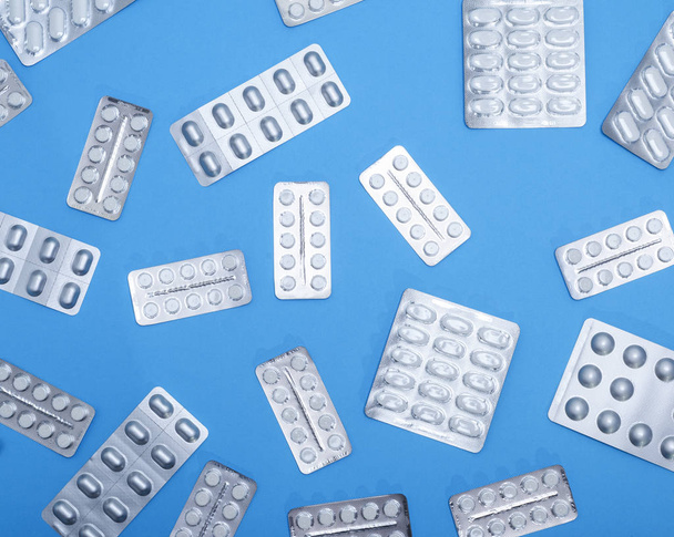 different white tablets in a package are scattered on a blue background, top view - Фото, зображення