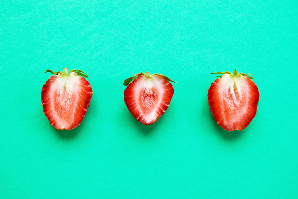 A row from halves of red ripe strawberry on a bright turquoise background, top view. Healthy summer food. - Fotó, kép