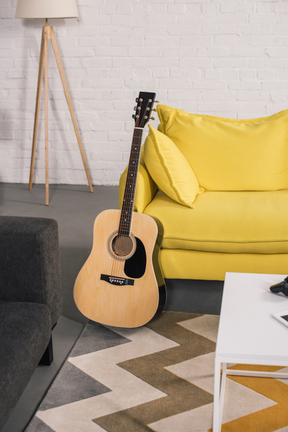 акустическая гитара возле уютного желтого дивана в современном интерьере
 - Фото, изображение
