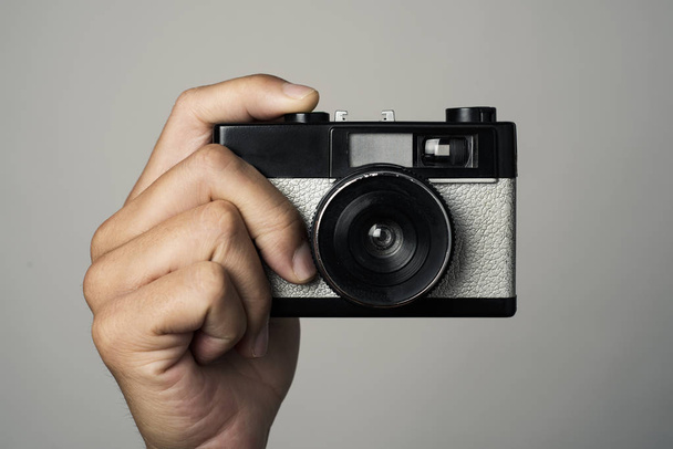 closeup of a caucasian man with a retro film camera in his hand, pointing to the obserever, about to press the shutter button, against an off-white background - Fotó, kép
