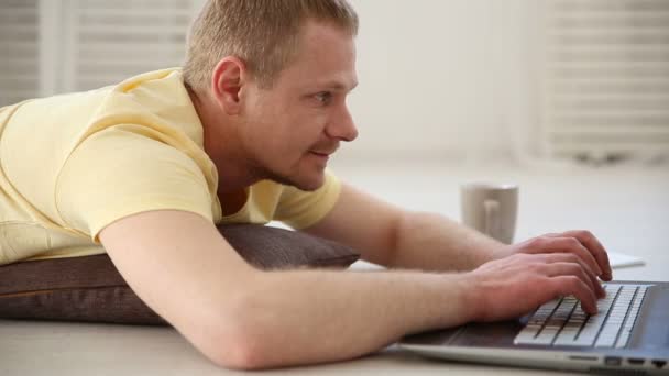 een freelance man aan het werk thuis op de vloer achter een laptop - Video