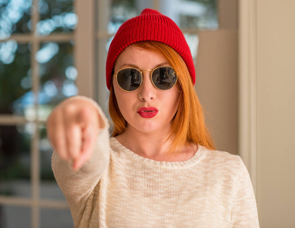 Elegante donna rossa con berretto di lana e occhiali da sole che punta con il dito alla fotocamera e a te, segno della mano, gesto positivo e fiducioso dal davanti
 - Foto, immagini