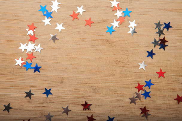 Конфітті зірки на дерев'яному фоні. 4 липня, День Незалежності, картка, запрошення в кольорах прапора США. Вид зверху, порожній простір
. - Фото, зображення