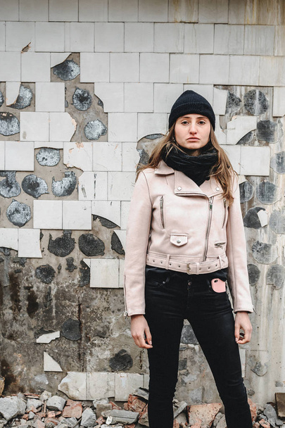 woman in black jeans, a hat and a pink jacket, in a dilapidated urban loft location. beauty fashion and style. mobile phone in a stylish case - Photo, image
