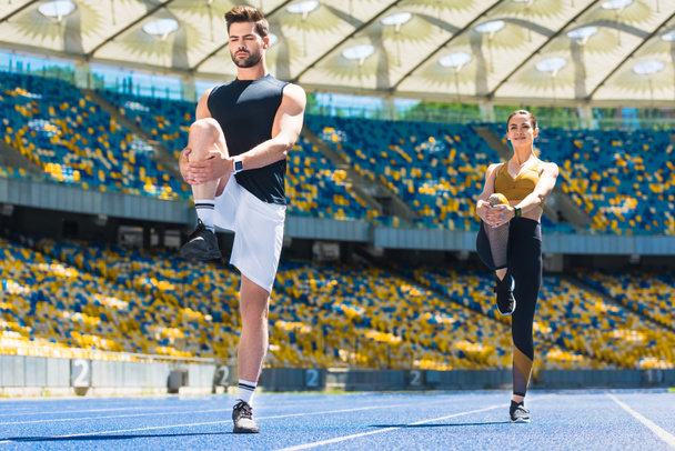 молодая спортивная пара разогревает ноги перед бегом по беговой дорожке на спортивном стадионе
 - Фото, изображение