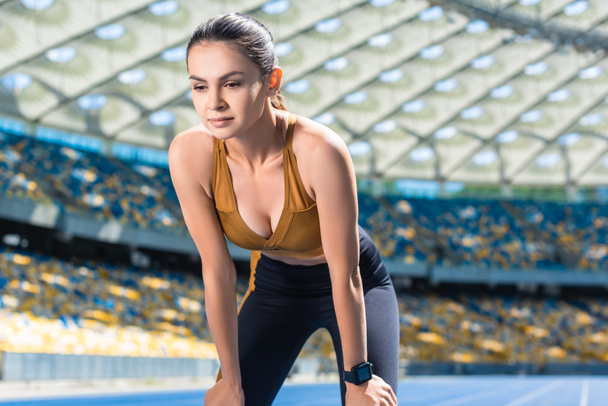Sportliche junge Frau ruht sich nach Joggen auf Laufstrecke am Sportstadion aus - Foto, Bild
