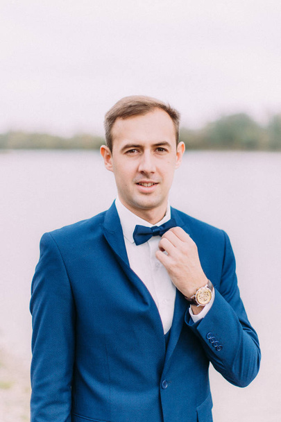 Close-up portrait of the groom corresting his bow-tie. - Zdjęcie, obraz