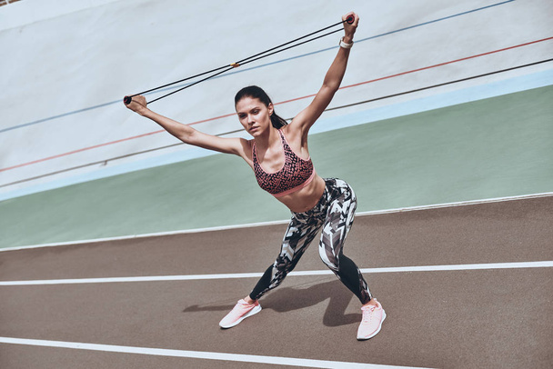 woman in sports clothing exercising with resistance band on running track stadium  - 写真・画像