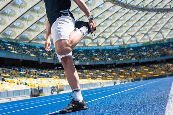 cropped shot of man stretching on running track at sports stadium - Foto, afbeelding